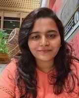 Headshot of a person with long, dark hair, wearing a coral-colored top, looking at the camera with a neutral expression.