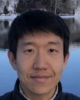 Headshot of a young man with short dark hair, smiling slightly, in front of a snowy lakeside scene.