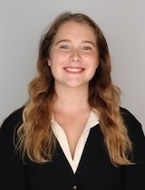 A smiling young woman with long wavy brown and blonde hair wears a black top over a white shirt.