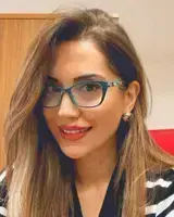 Smiling woman with long brown hair, wearing teal glasses and red lipstick.